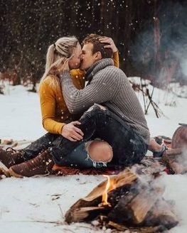 Парень целует девушку в лесу зимой возле костра - картинка